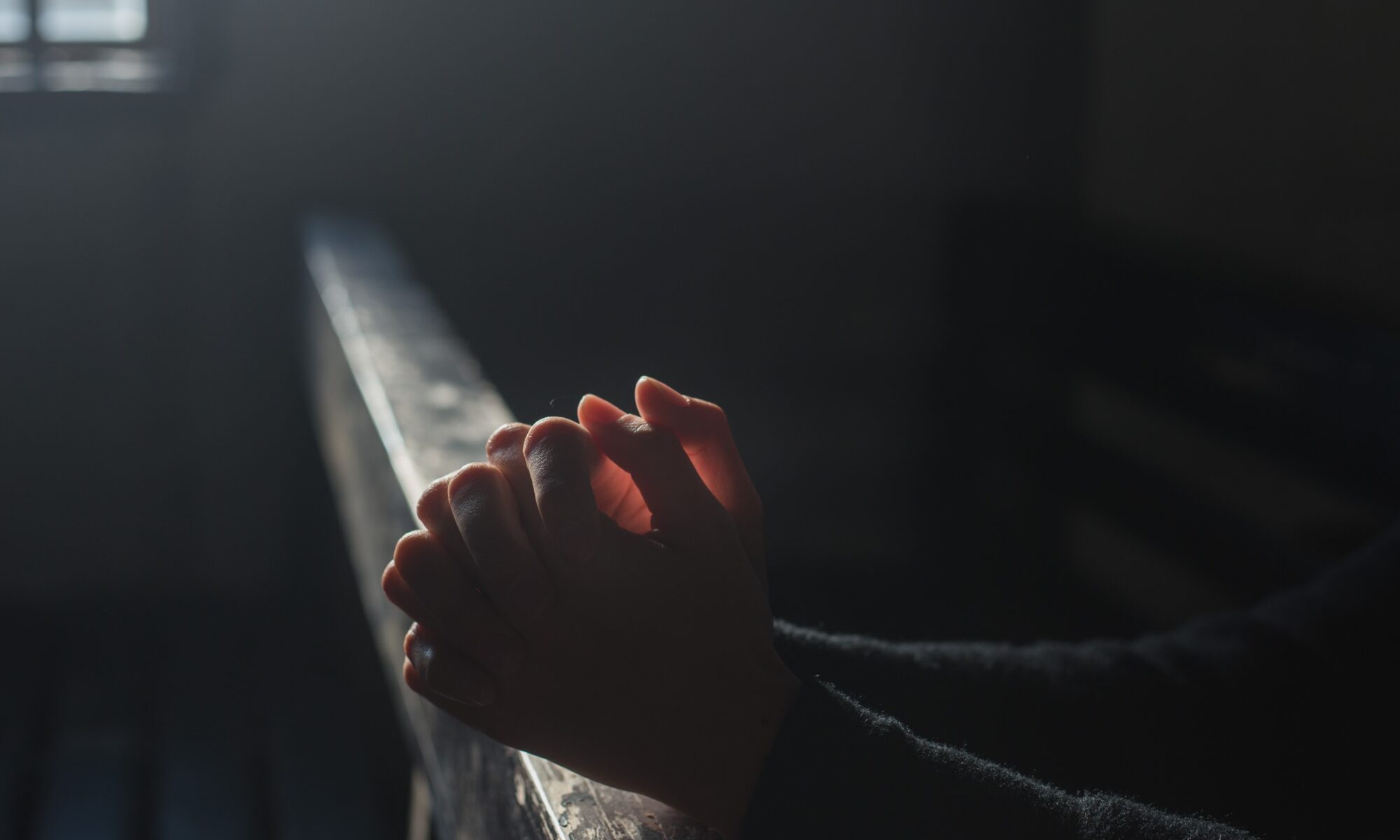 Deux mains jointes en prière sur le dossier d'un banc d'église